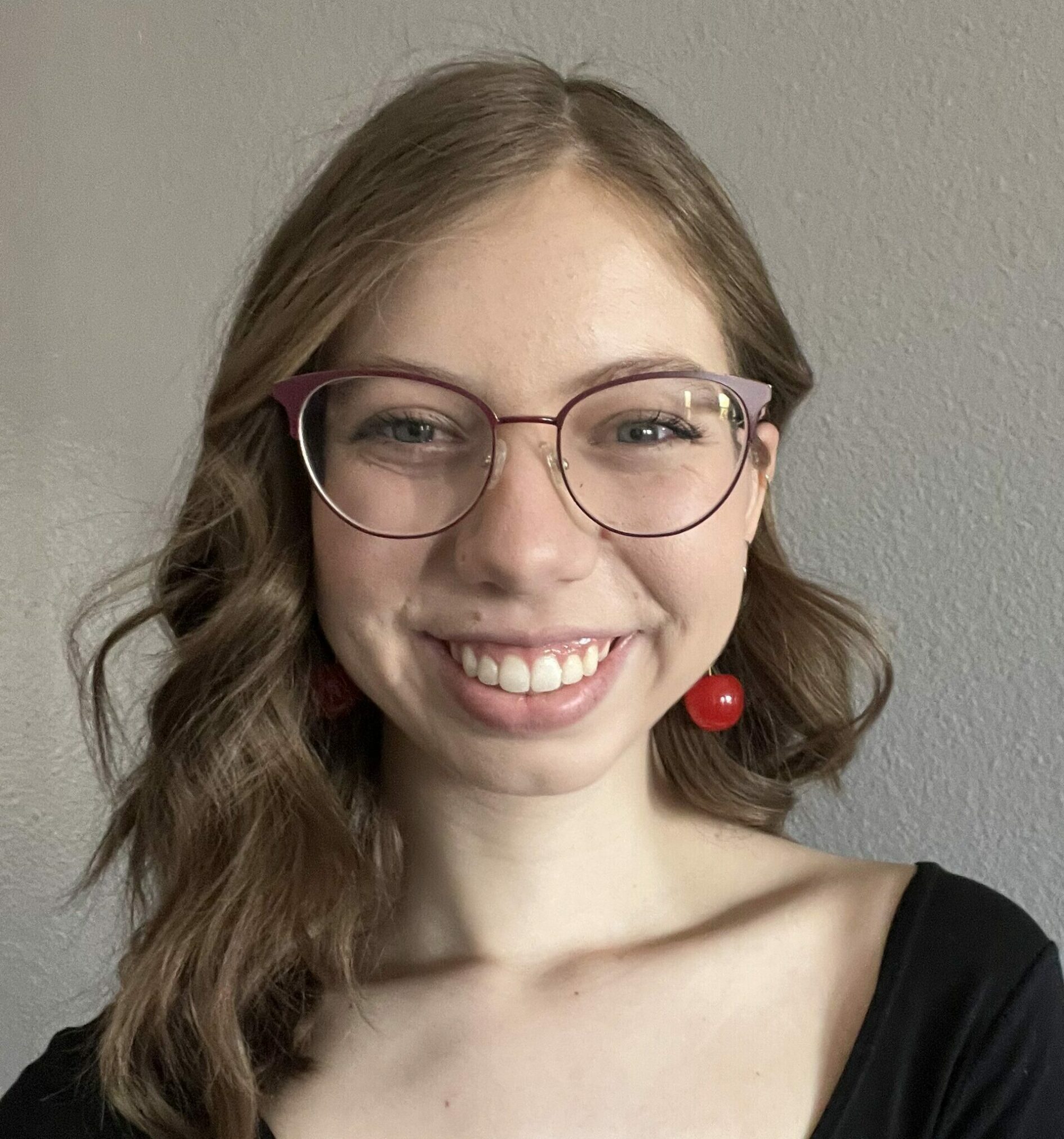 Headshot of Amanda Behmer with glasses, wearing a black top and red earrings, smiling at the camera.