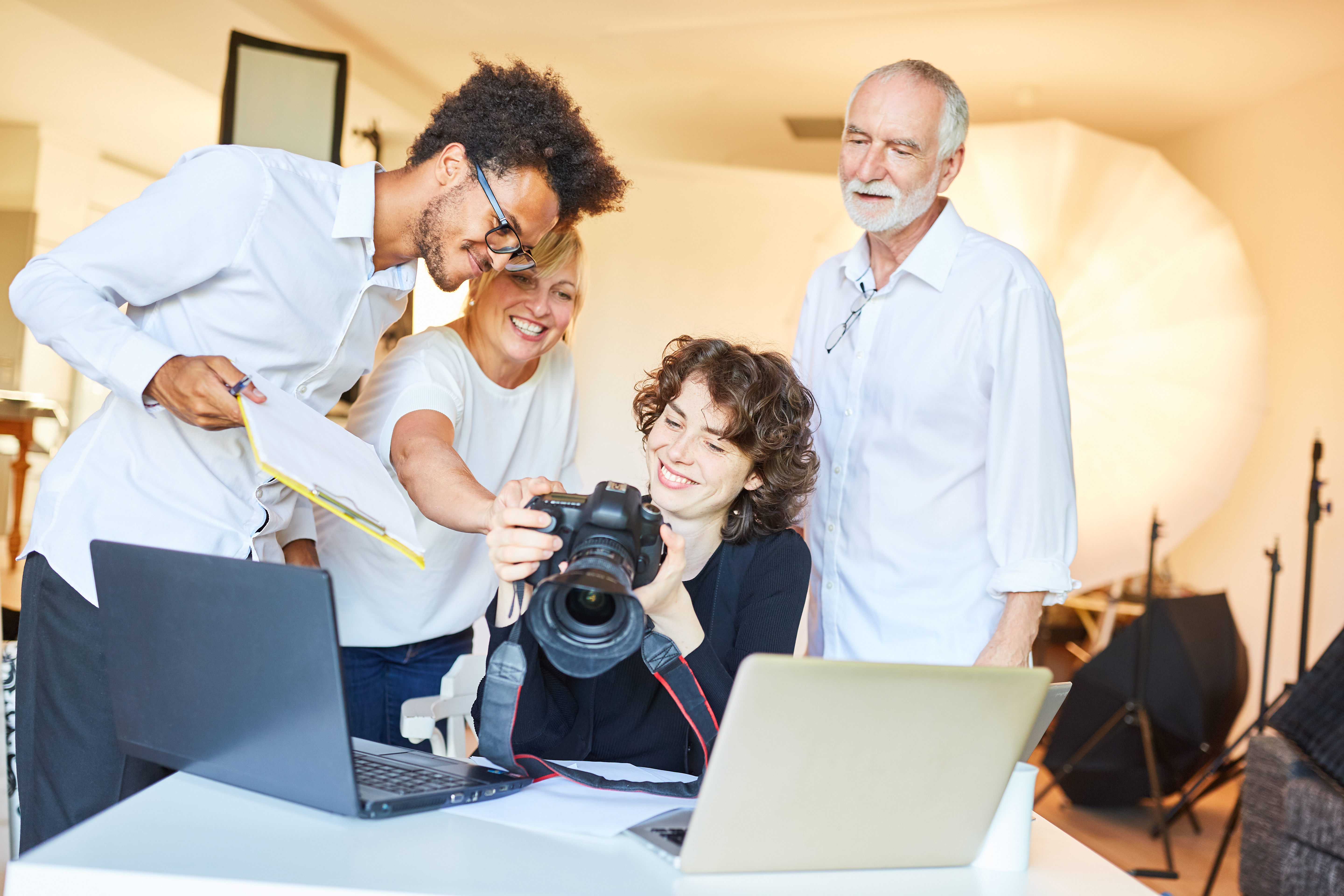 Four people in a photography studio smile and look inquisitively upon a professional camera